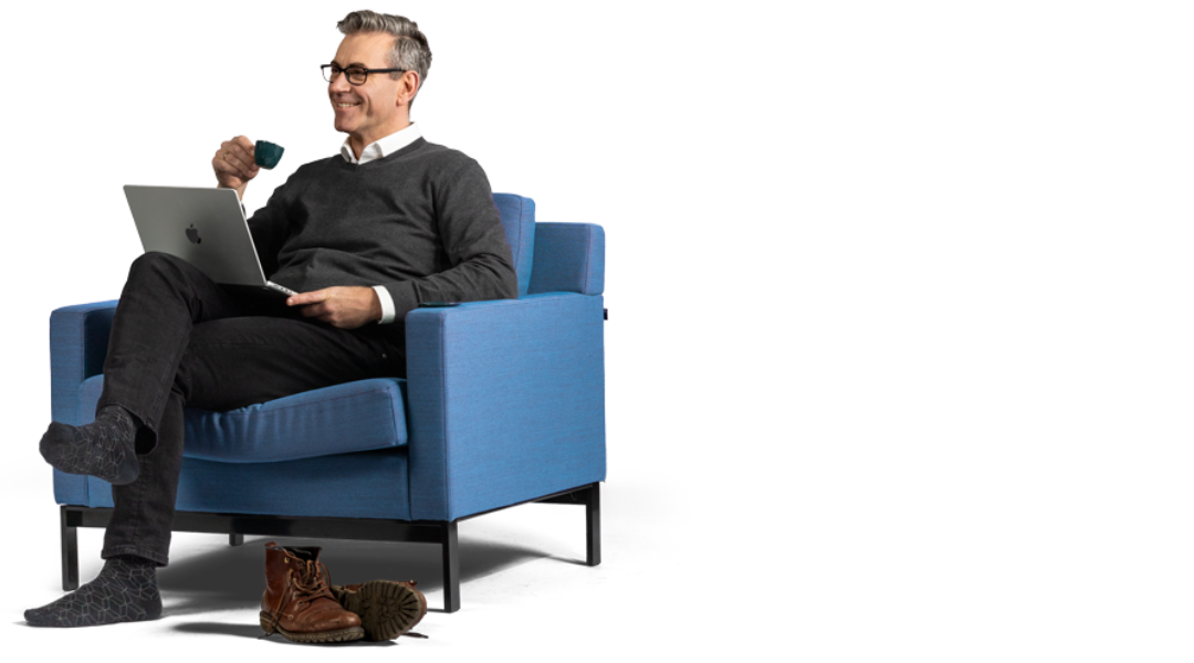 Een man met een kop koffie en een laptop in een blauwe fauteuil